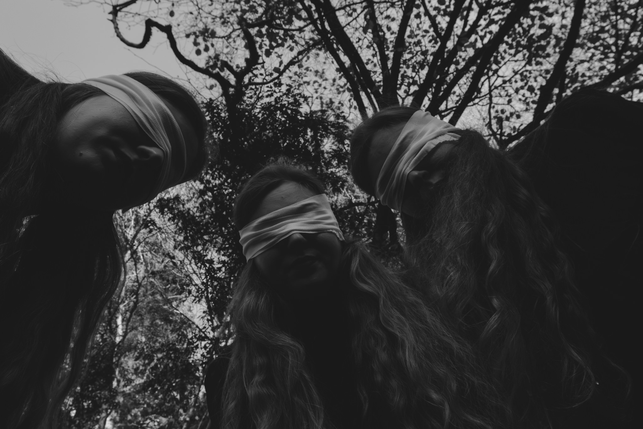 Three women in black standing over you POV with white eye coverings in the woods